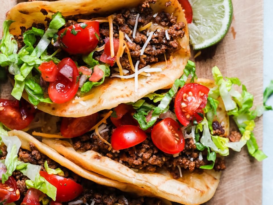 crispy beef tacos with cheese, shredded lettuce, tomatoes, and lime