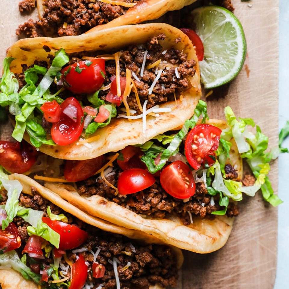 crispy beef tacos with cheese, shredded lettuce, tomatoes, and lime