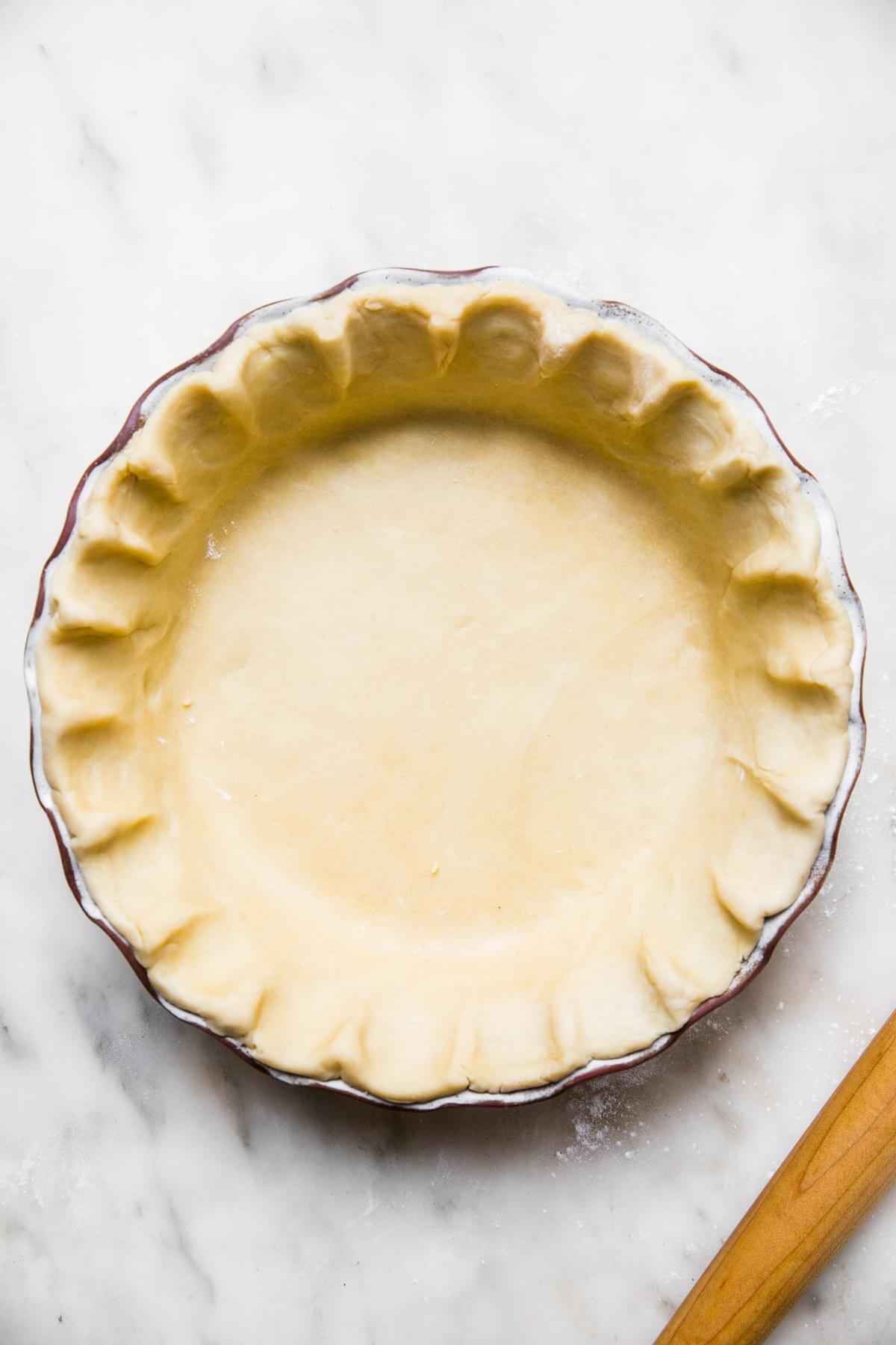 homemade easy all-butter pie crust in a pie pan next to a rolling pin