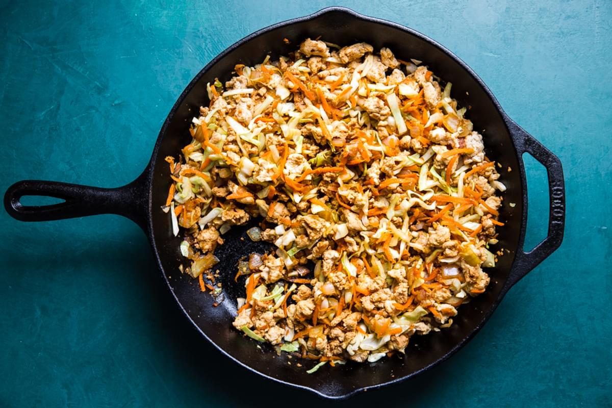 egg roll ingredients, ground turkey, onions, garlic and ginger in a cast iron skillet