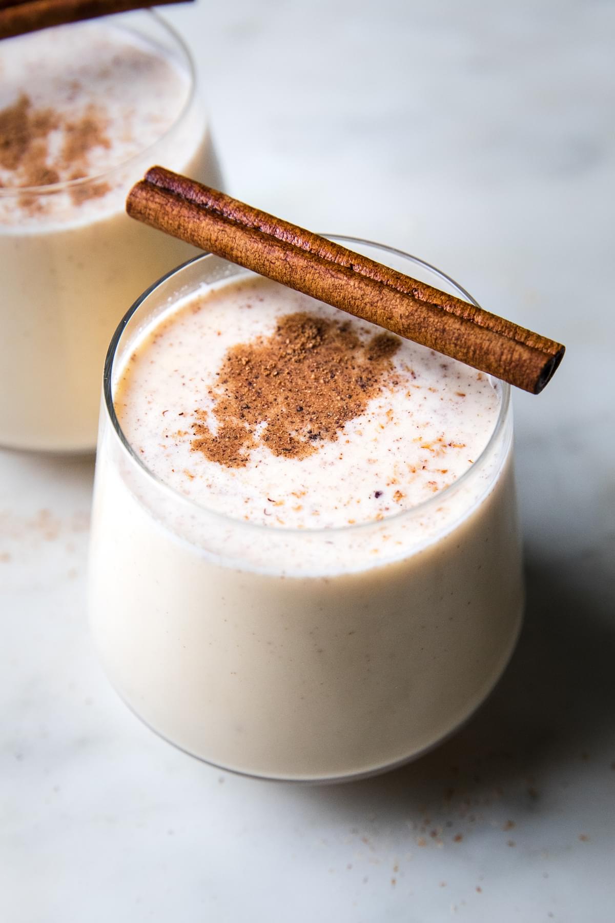 homemade eggnog in glasses with a dusting of nutmeg and a cinnamon stick