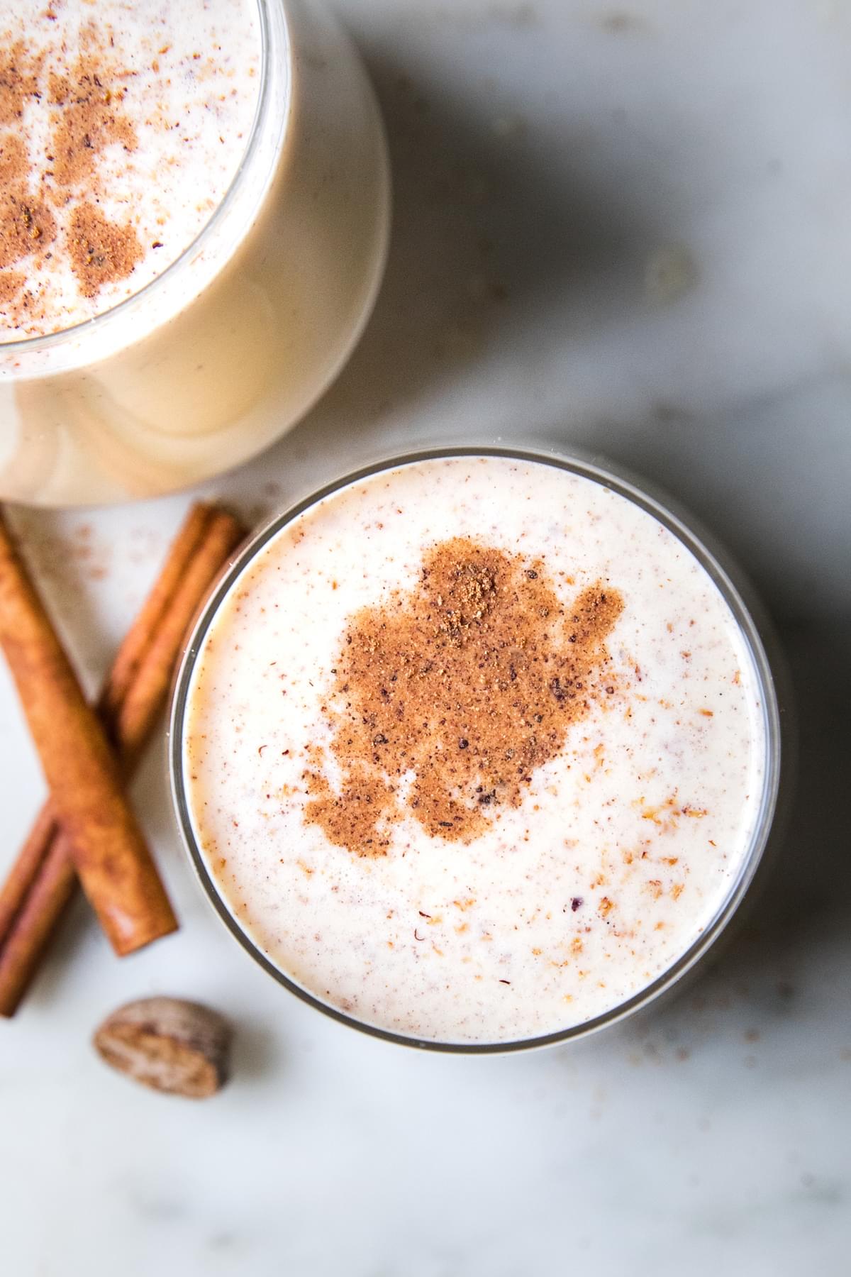 homemade eggnog in glasses with a dusting of nutmeg and a cinnamon stick