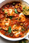 Homemade fish puttanesca made with cod, olives, tomatoes and parsley in a braising pot