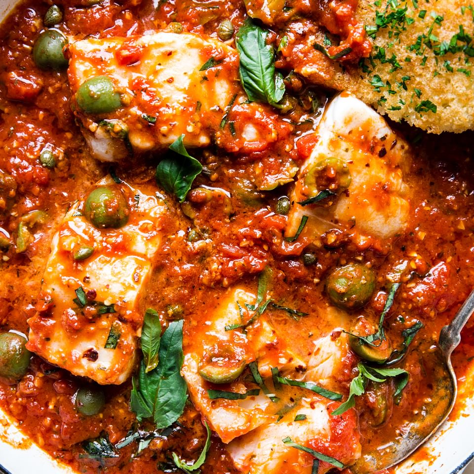 Homemade fish puttanesca made with cod, olives, tomatoes and parsley in a braising pot
