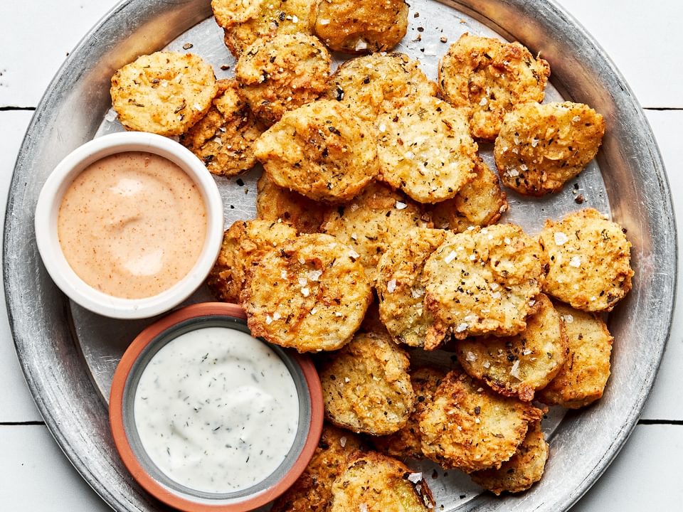 homemade fried pickles on a serving plate with bowls of ranch dressing and fry sauce for dipping