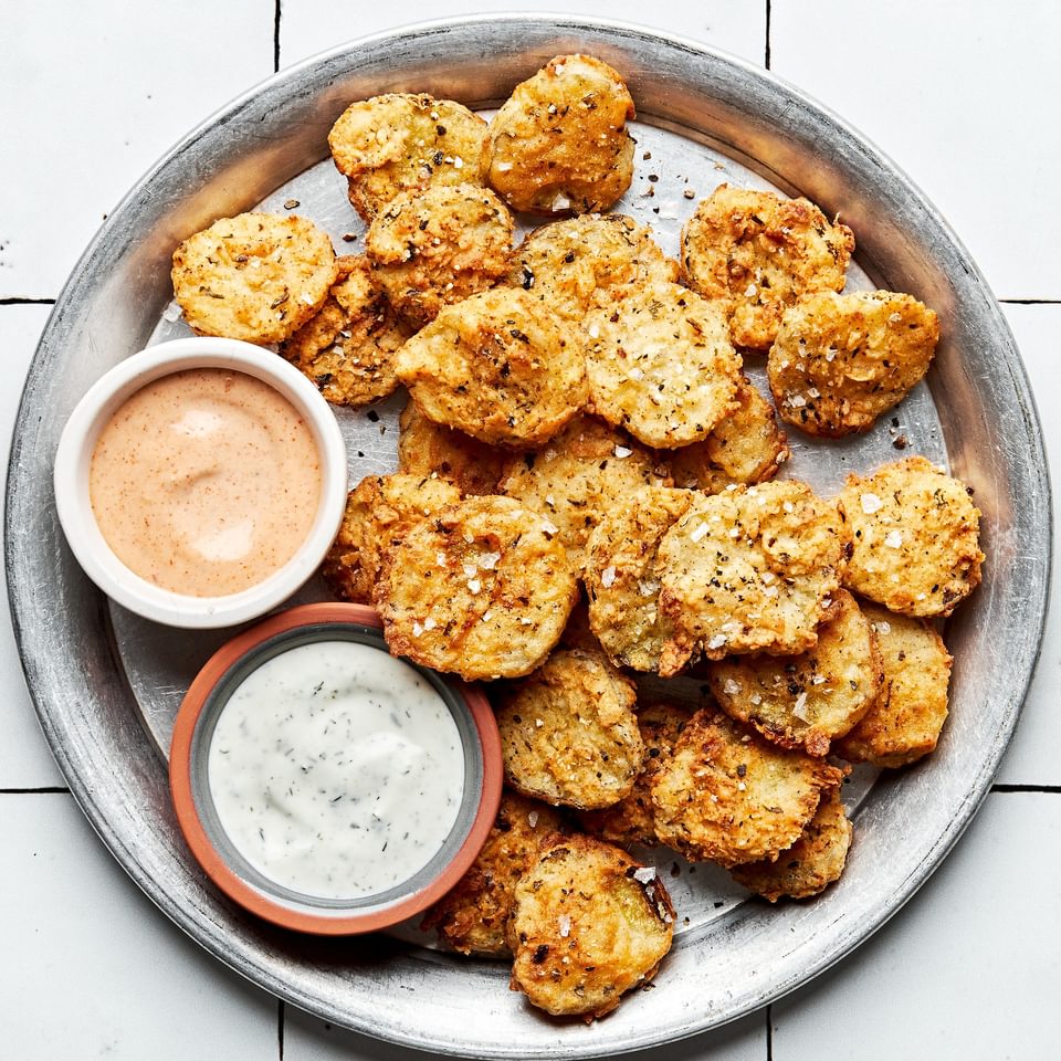 homemade fried pickles on a serving plate with bowls of ranch dressing and fry sauce for dipping