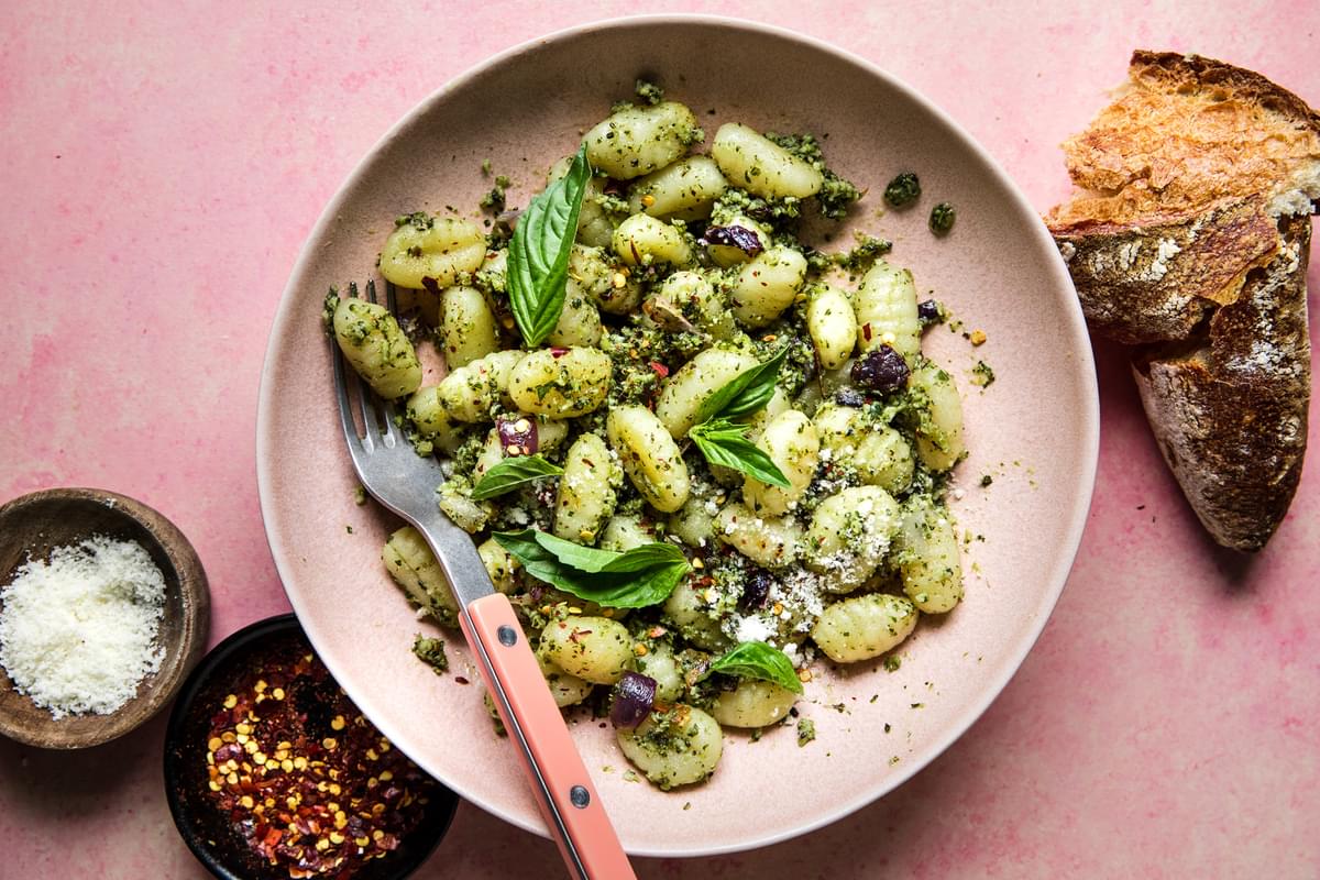 Roasted broccoli pesto gnocchi with red onions in a bowl with parmesan and red pepper flakes