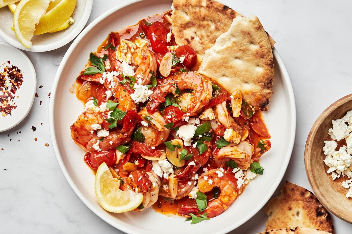 Greek shrimp on a plate topped with parsley, lemon juice and feta served with pita bread