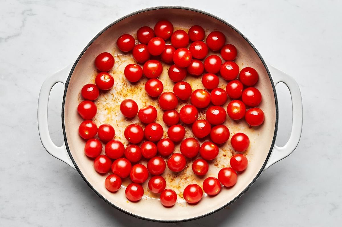 cherry tomatoes being cooked in a skillet with olive oil