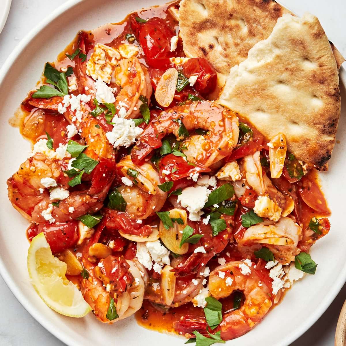 greek shrimp on a plate topped with parsley, lemon juice and feta served with pita bread
