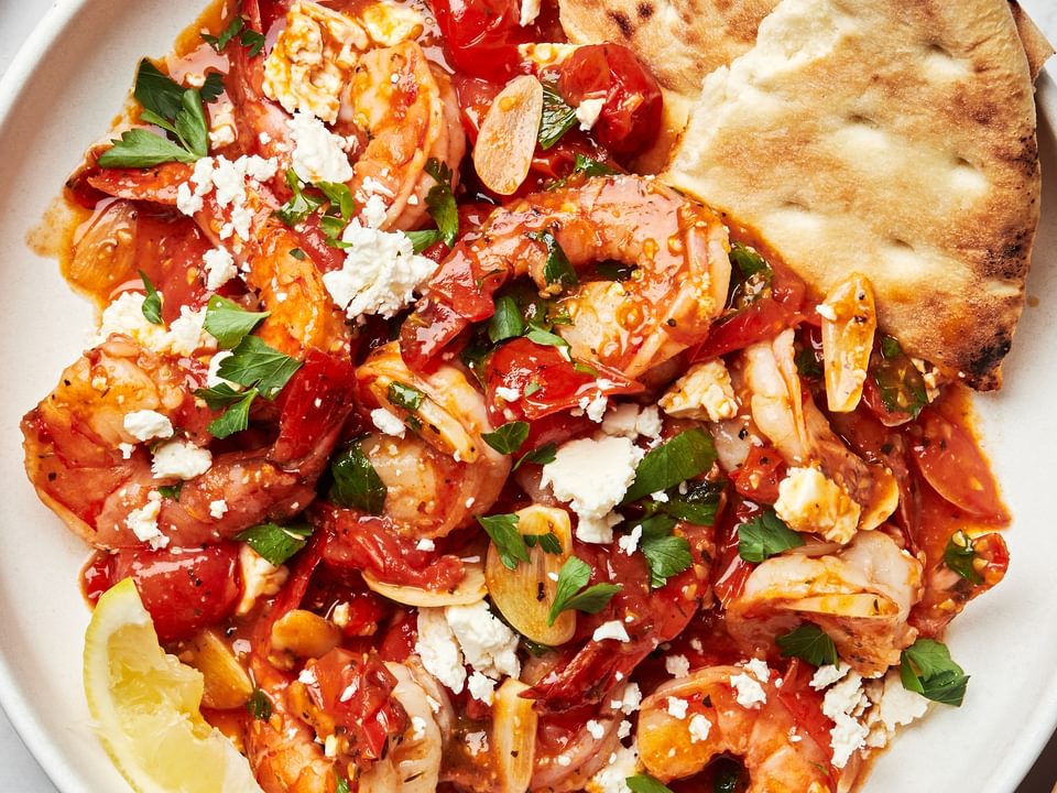greek shrimp on a plate topped with parsley, lemon juice and feta served with pita bread