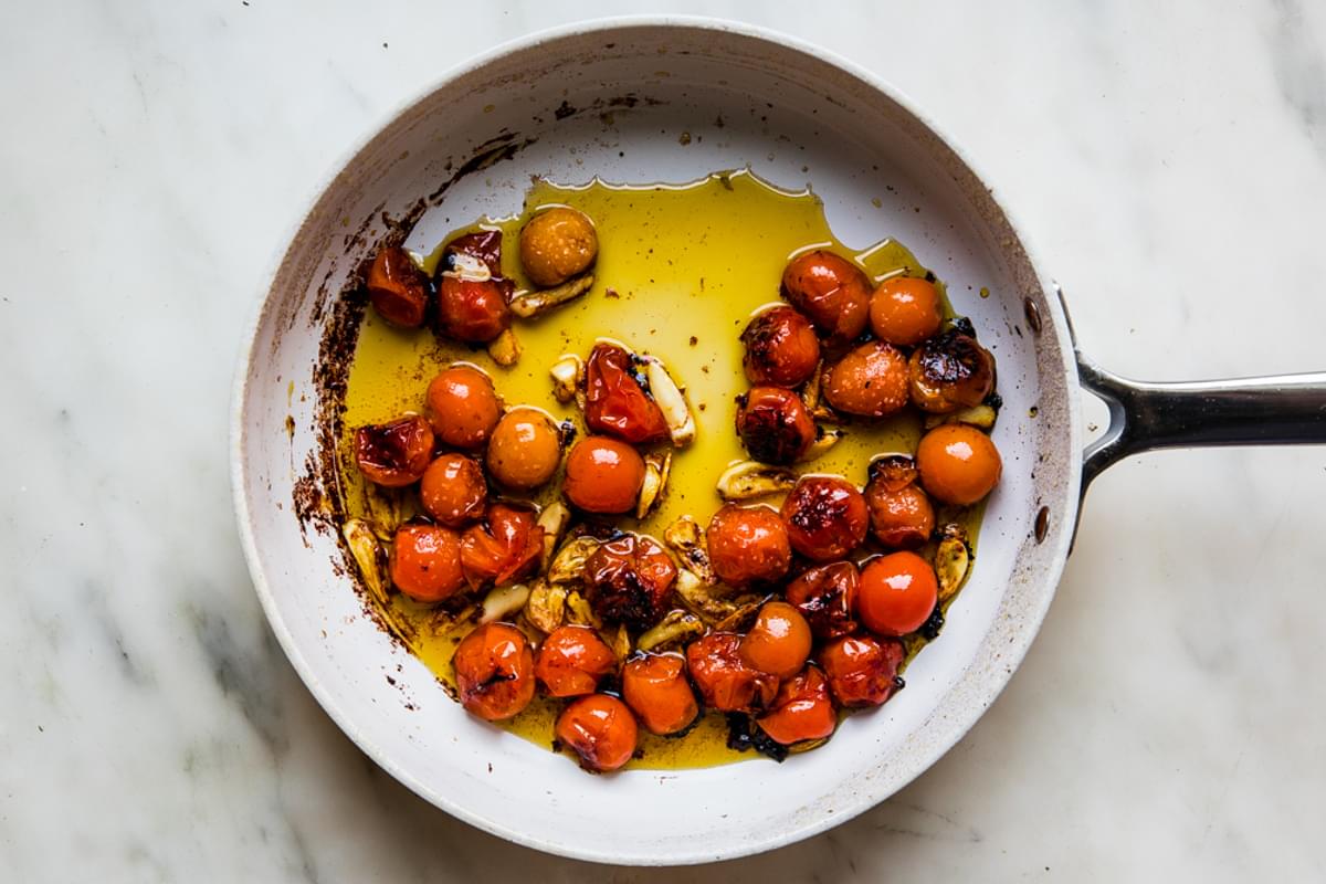 blistered cherry tomatoes in a skillet with olive oil and garlic