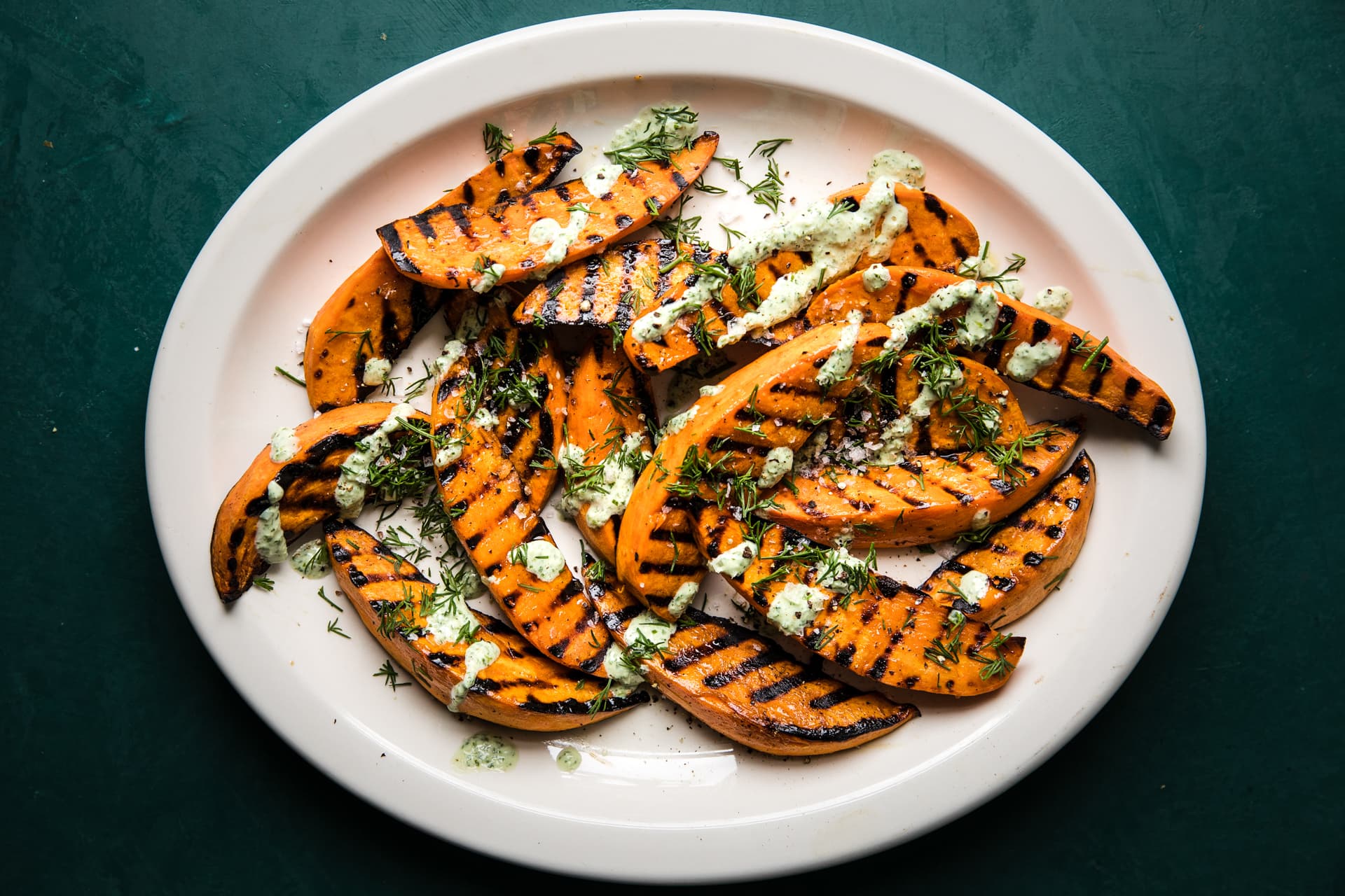Grilled Sweet potatoes with olive oil and sea salt on a plate drizzled with a basil & dill yogurt sauce