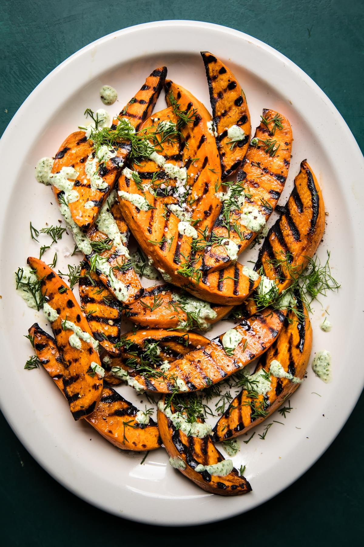 Grilled Sweet potatoes with olive oil and sea salt on a plate drizzled with a basil & dill yogurt sauce