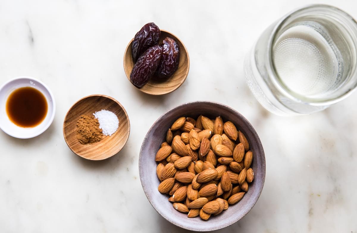 almonds, dates, vanilla extract, cinnamon, salt and filtered water in bowls on the counter for making homemade almond milk