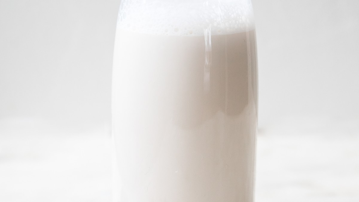 Homemade almond milk in a carafe on the counter surrounded by almonds and dates
