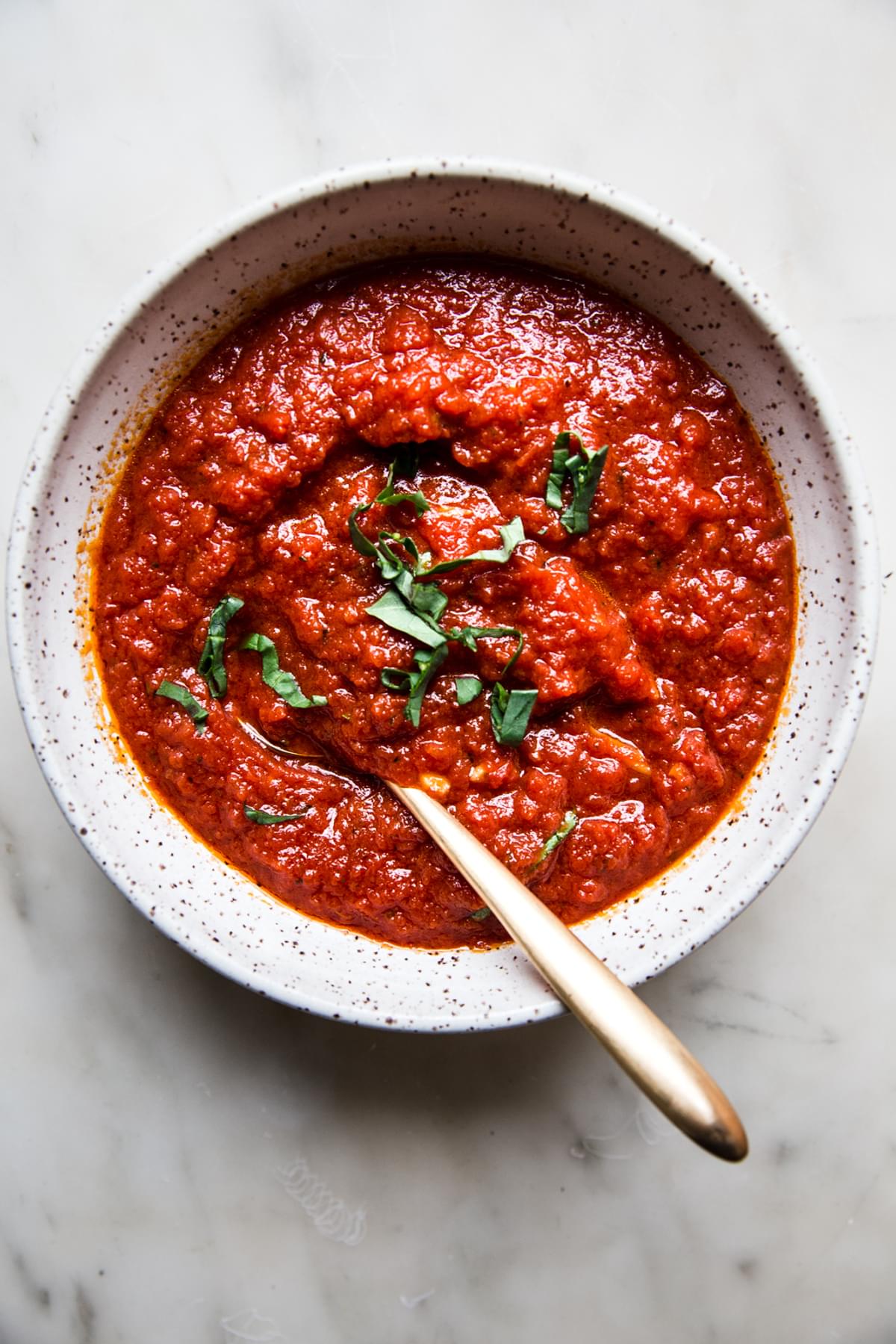Homemade Marinara Sauce in a bowl with a spoon and fresh basil