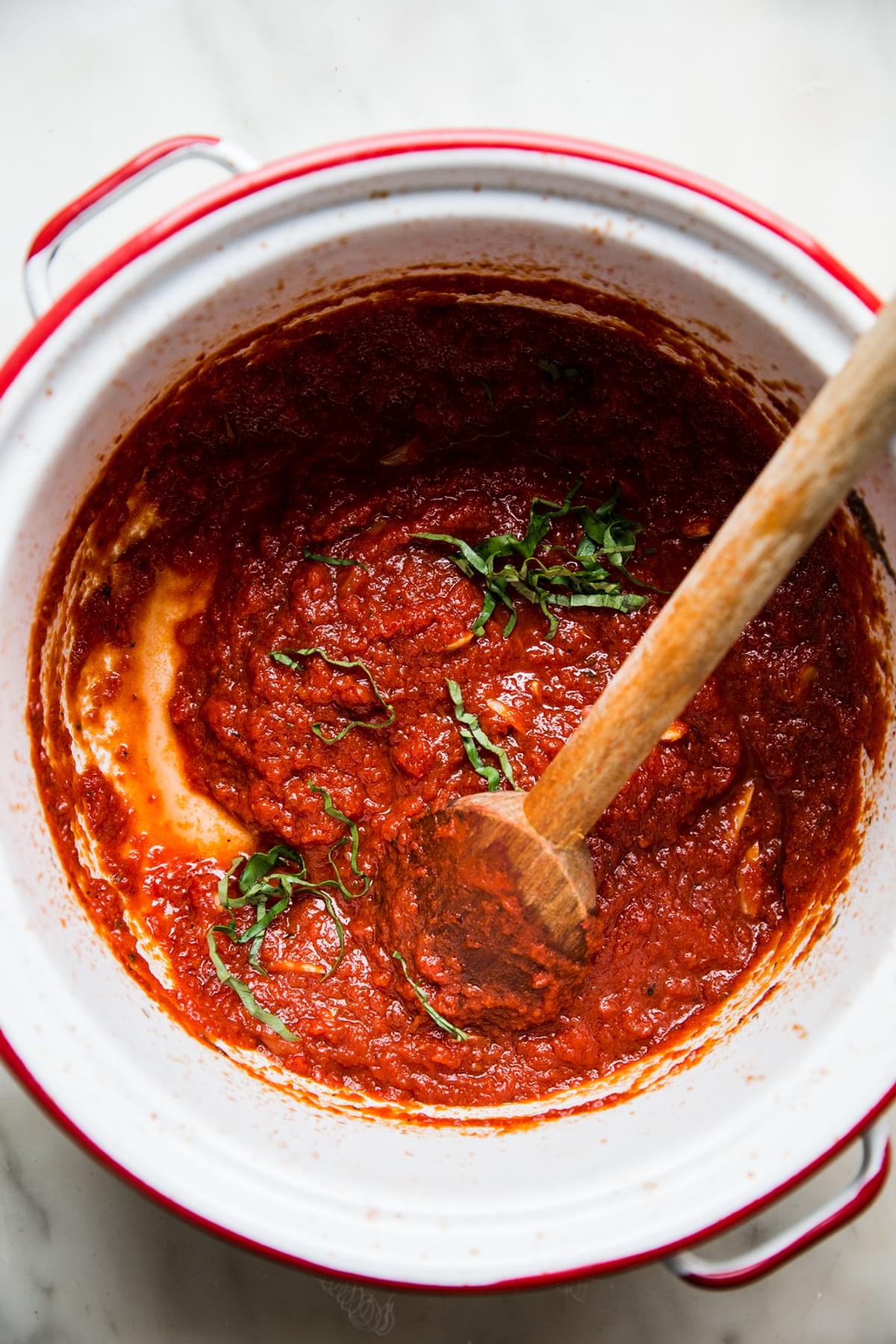 Homemade Marinara Sauce being stirred in a pot with basil
