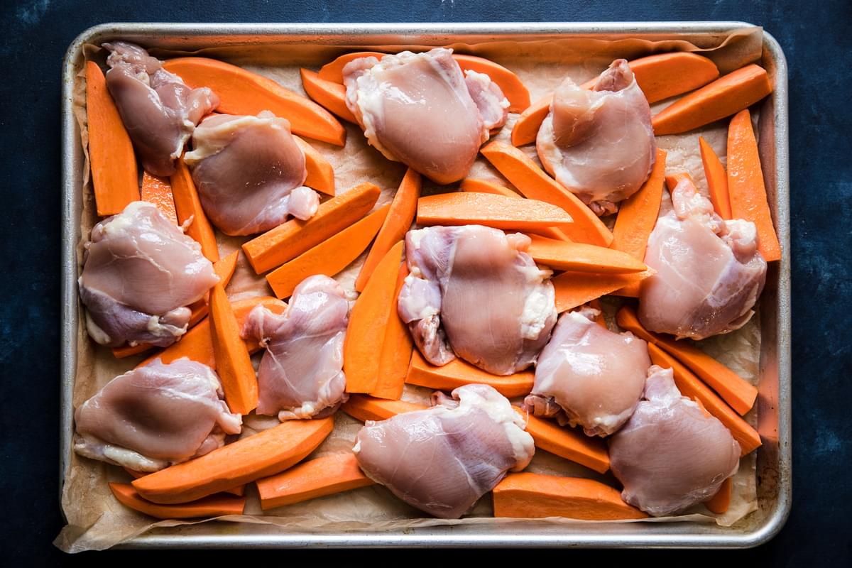 boneless skinless chicken thighs and sweet potato wedges on a sheet pan