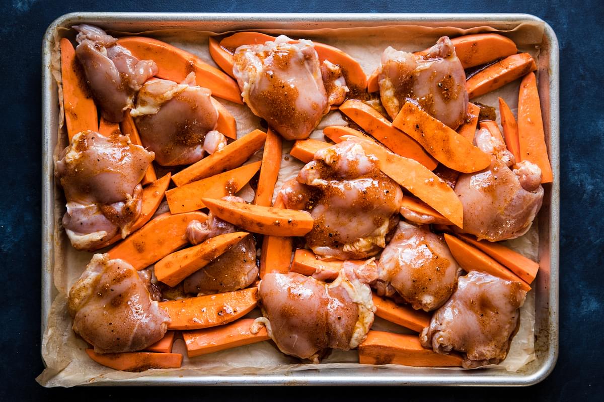 chicken thighs and sweet potato wedges on a sheet pan with chili-honey marinade
