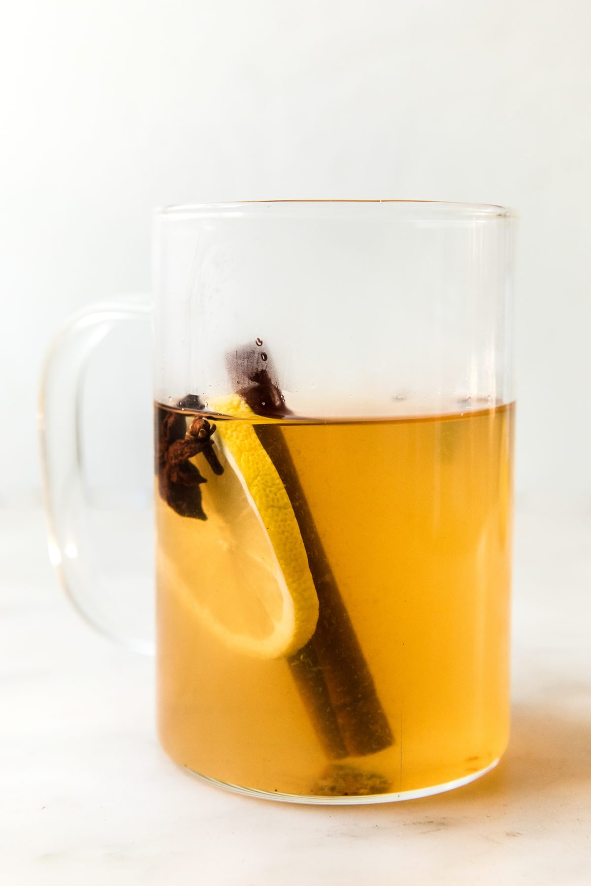 homemade hot toddy recipe with a lemon slice and cinnamon stick in a mug on the counter