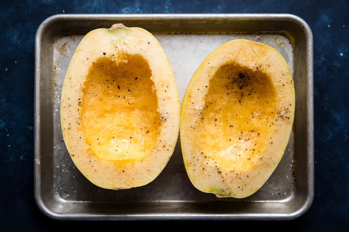 a spaghetti squash cut open on a baking sheet with salt and pepper