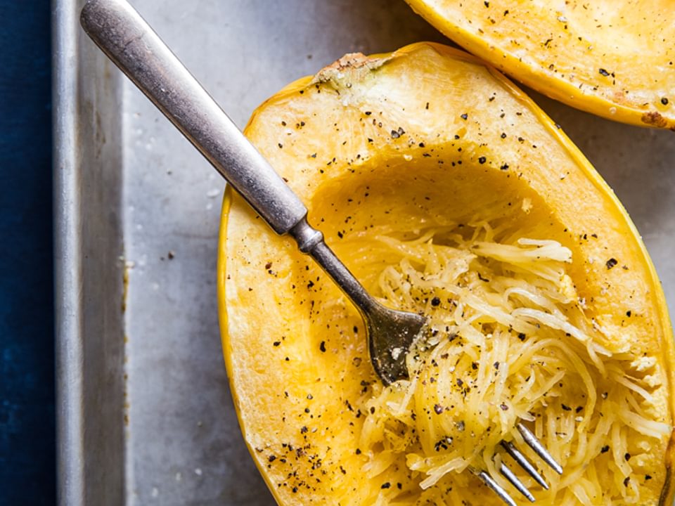 spaghetti squash cut open and roasted on a baking sheet with a fork, salt and pepper