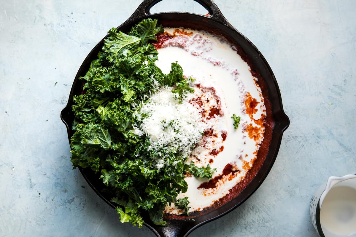 tomato sauce in a cast iron skillet with heavy cream, parmesan cheese and kale