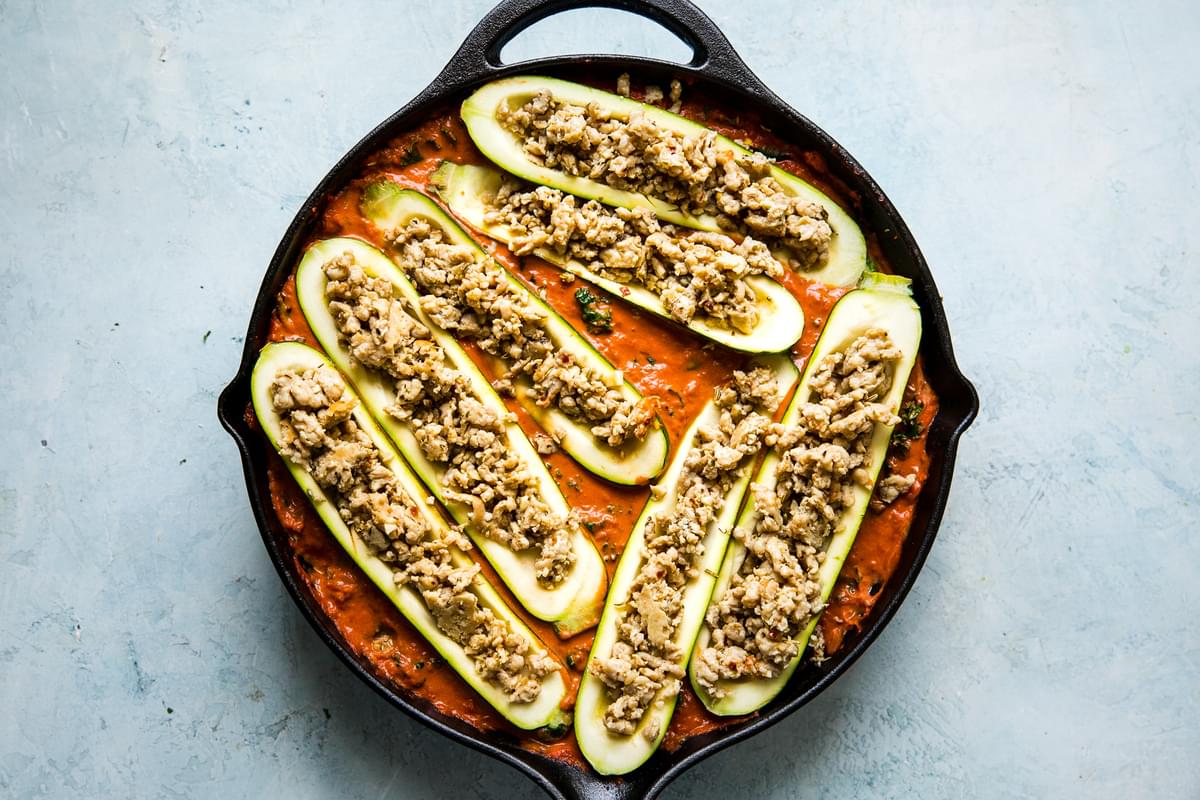 zucchini boats with ground chicken and spices in a creamy tomato sauce in a skillet