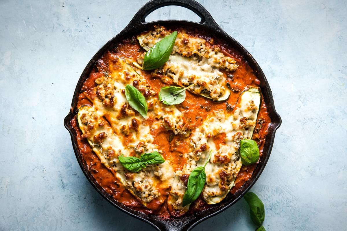 zucchini boats with ground chicken, spices, parmesan cheese, mozzarella and basil in a creamy tomato sauce in a skillet