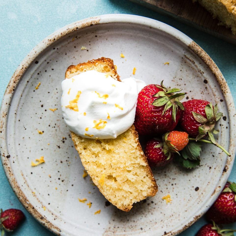 Olive Oil Cake made with lemon topped with whipped cream and berries on a plate