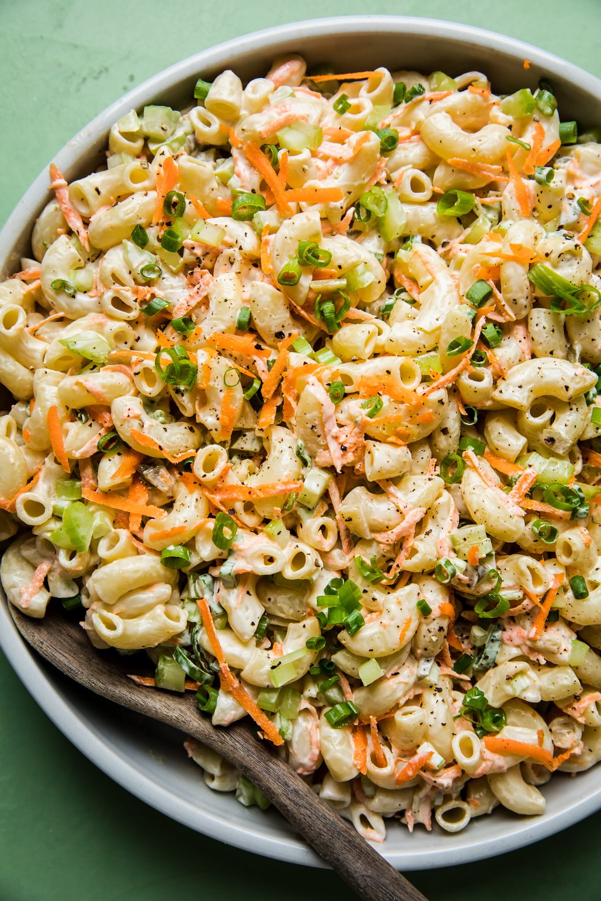 a bowl of homemade macaroni salad in a bowl with carrots, celery and green onions