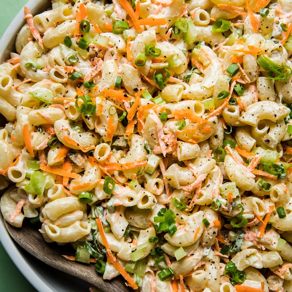 a bowl of homemade macaroni salad in a bowl with carrots, celery and green onions