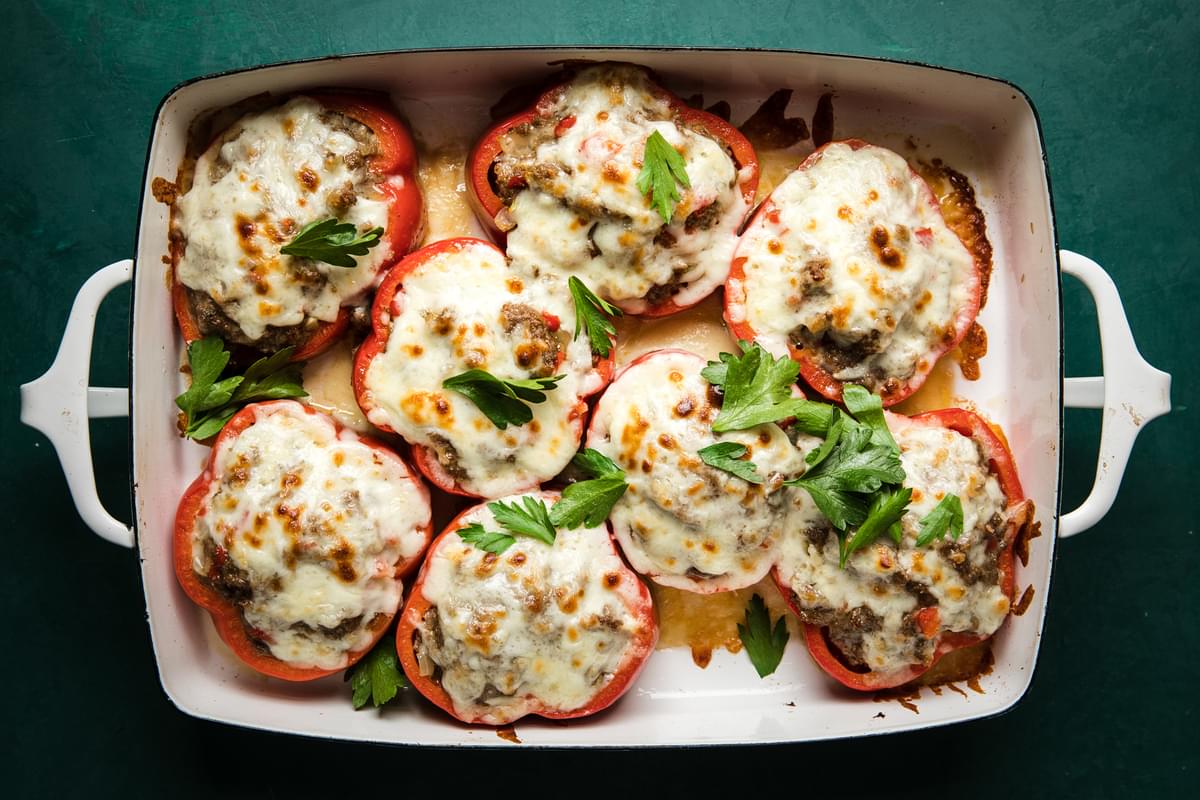 Homemade Meatball Stuffed Peppers topped with melted cheese and parsley garnish in a baking dish on the counter