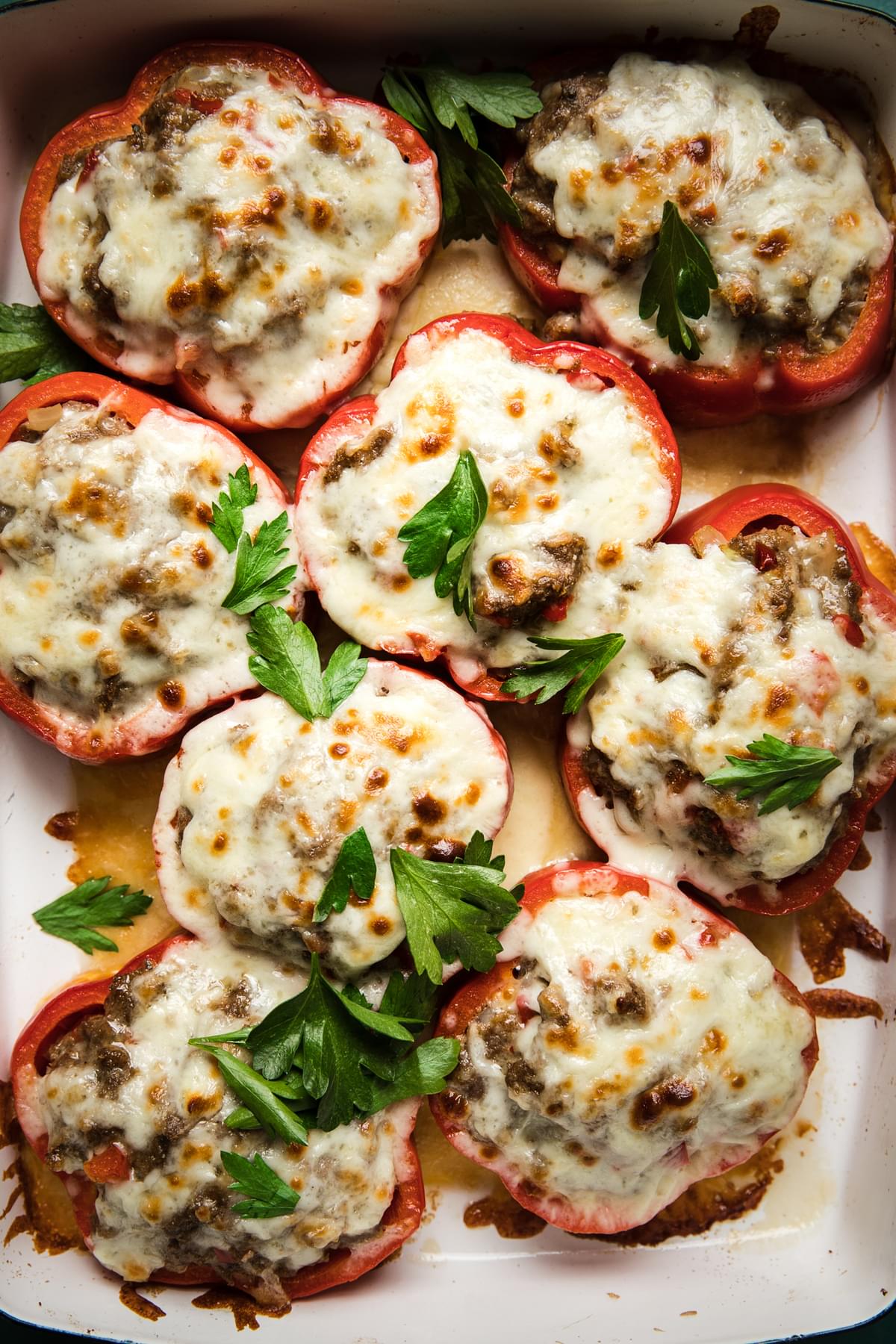 Homemade Meatball Stuffed Peppers topped with melted cheese and parsley garnish in a baking dish