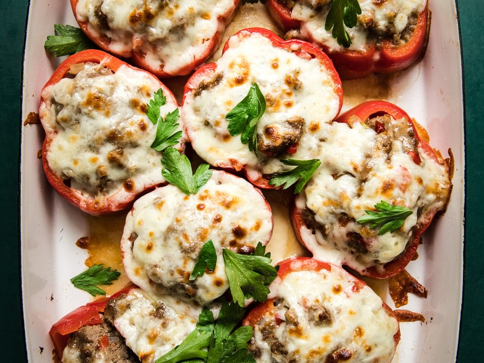 Homemade Meatball Stuffed Peppers topped with melted cheese and parsley garnish in a baking dish