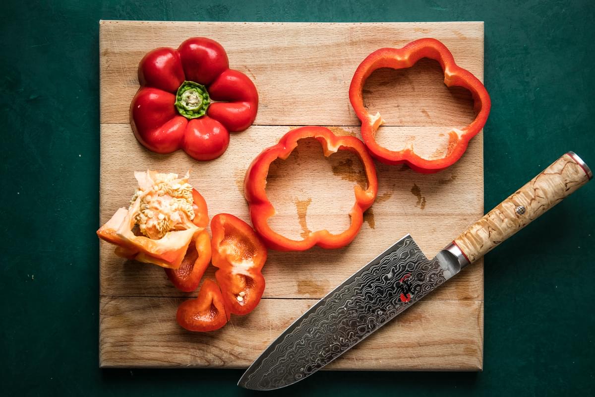 bell peppers with tops and bottoms cut off and cut into 2 rings on a cutting board with a knife