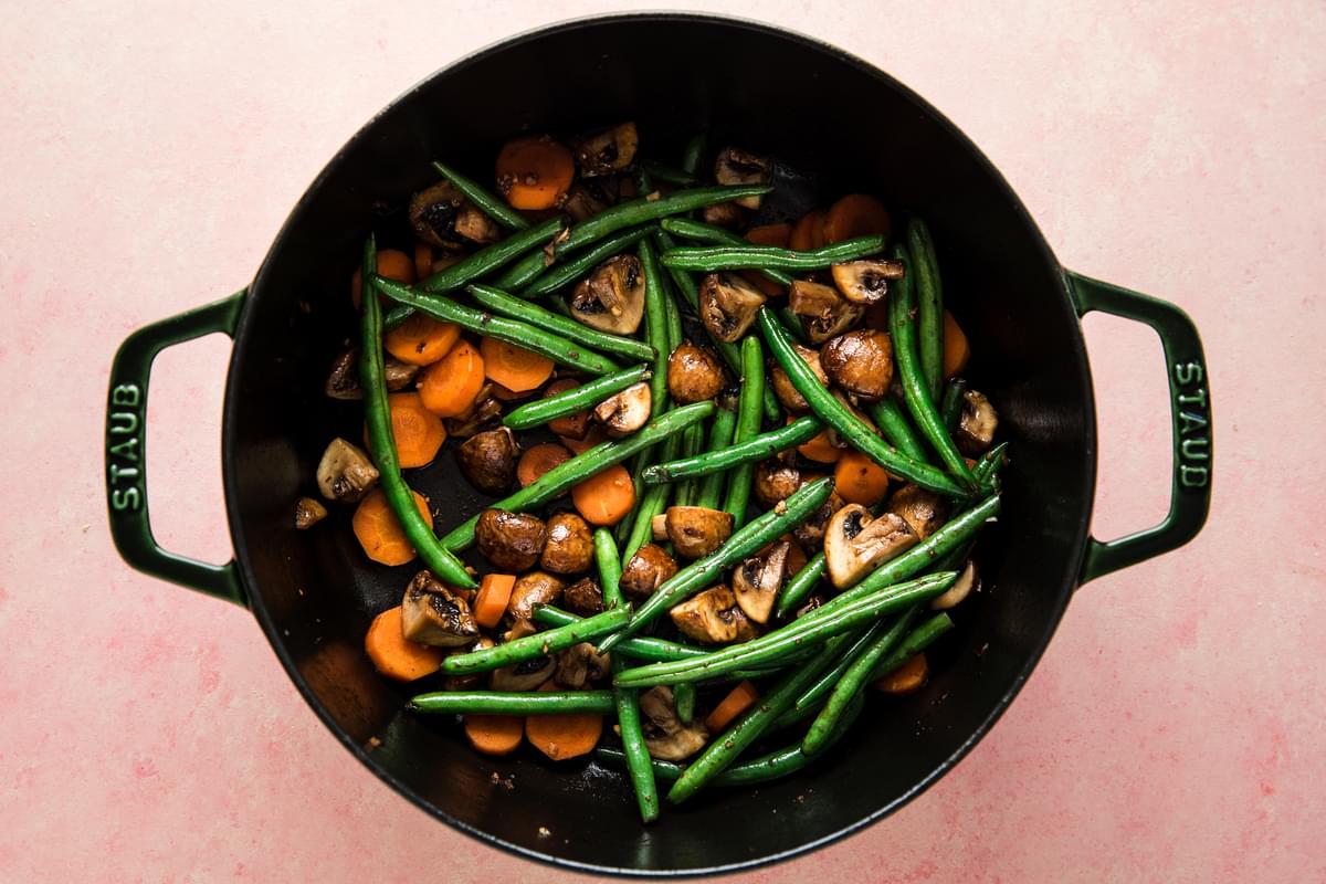 green beans, carrots, and mushrooms, oil, garlic and salt in a dutch oven ready to be sautéed
