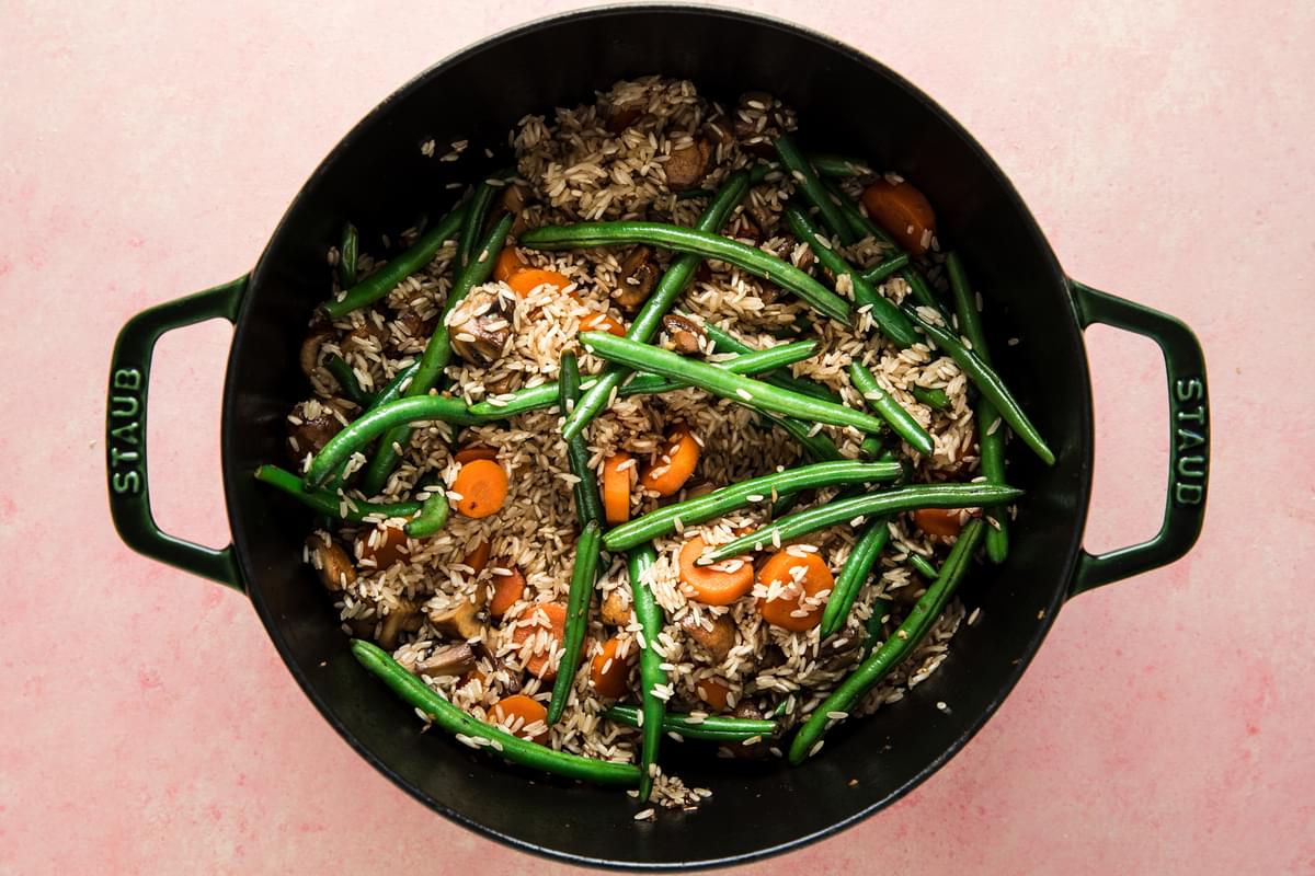 sautéed green beans, carrots, and mushrooms in a dutch oven with uncooked rice