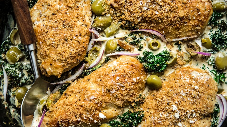 chicken breast with creamed kale topped with Castelvetrano  olives and toasted panko breadcrumbs in a skillet
