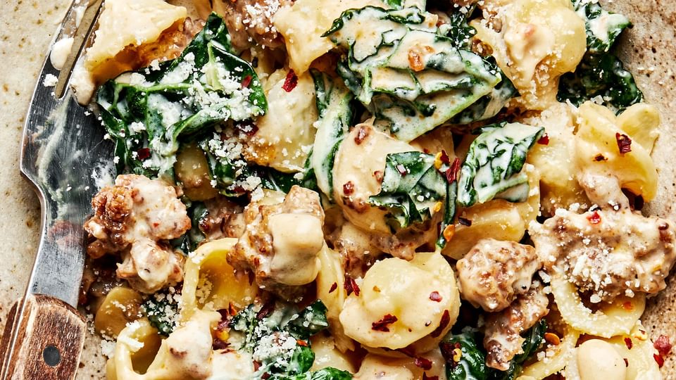 Orecchiette pasta with kale and sausage in a large bowl with a fork.