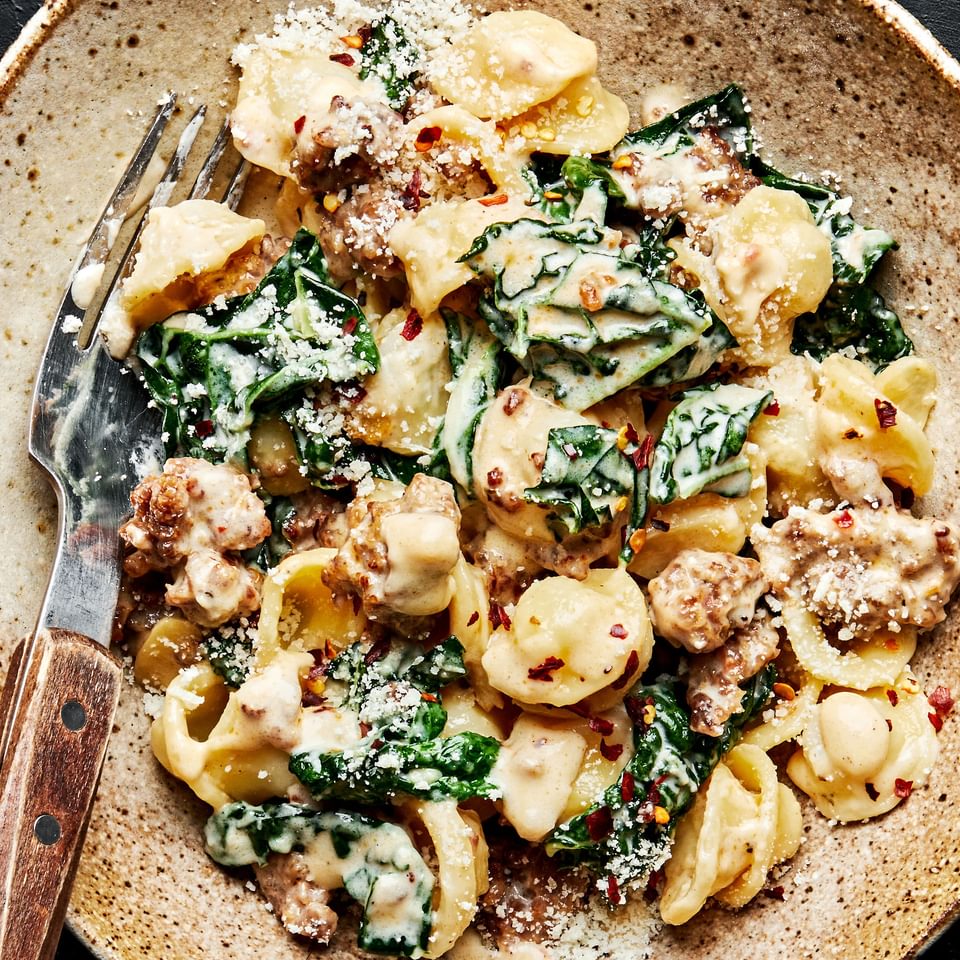 Orecchiette pasta with kale and sausage in a large bowl with a fork.