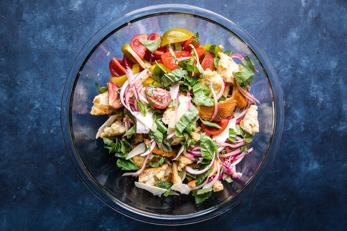 tomatoes, pickled onions, basil, parmesan cheese, and toasted bread pieces tossed together in a bowl for panzanella salad