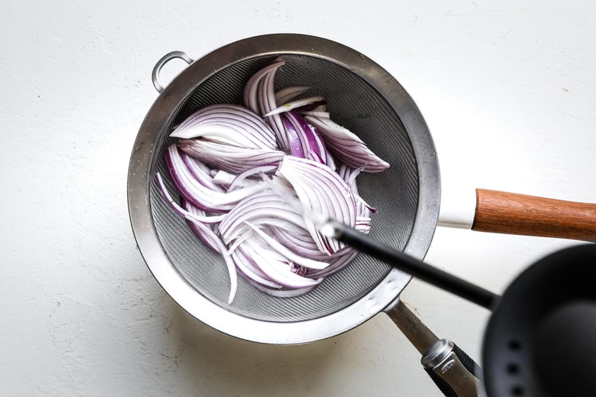 boiling water being poured over red onions in a strainer