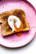Pink plate with a piece of toast and a poached egg with salt and pepper