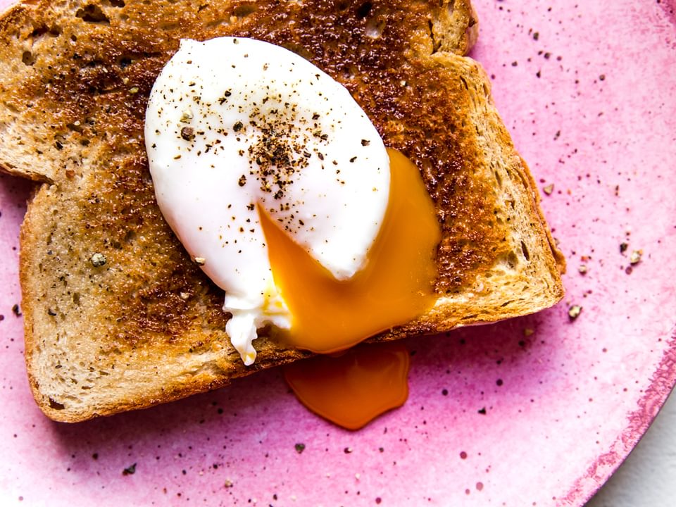 Pink plate with a piece of toast and a poached egg with salt and pepper
