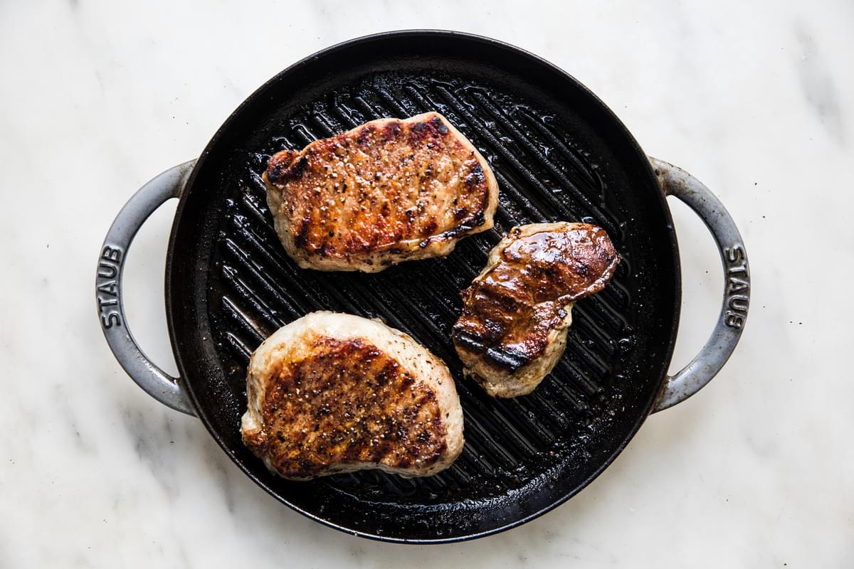 pork chops seasoned with salt, pepper, garlic powder, brown sugar and basil being cooked on a grill pan