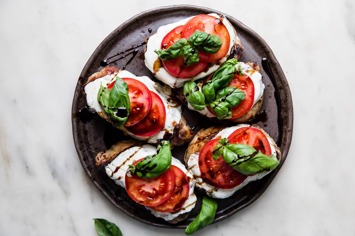 grilled pork chops topped with mozzarella, tomato slices, fresh basil and drizzled with balsamic glaze on a platter