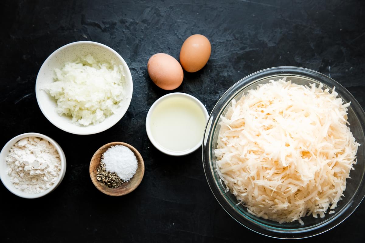potatoes, onions, flour, salt, pepper and eggs in bowls on the counter to make homemade latkes