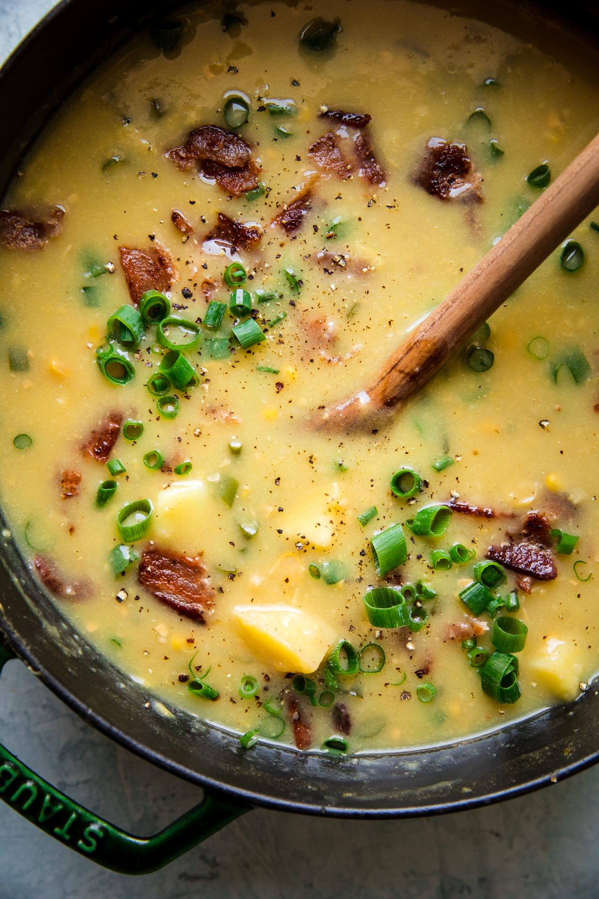 potato and corn chowder with bacon in a stock pot with a wooden spoon